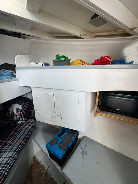 A white metal utility cabinet or storage box with two doors, shown in a tight, cluttered indoor space alongside shelves, a microwave, and other household items.