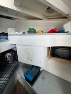A white metal utility cabinet or storage box with two doors, shown in a tight, cluttered indoor space alongside shelves, a microwave, and other household items.