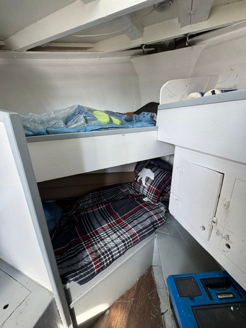 A close-up view inside a white storage compartment or drawer area, showing folded bedding or fabric items in dark plaid and blue tones, with part of a blue box visible at the upper right.