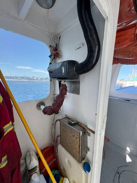 A close-up, angled view of the interior of a boat cabin, showing a black exhaust pipe, a rusty metal component, a yellow pole, and red life jackets in the foreground and background.