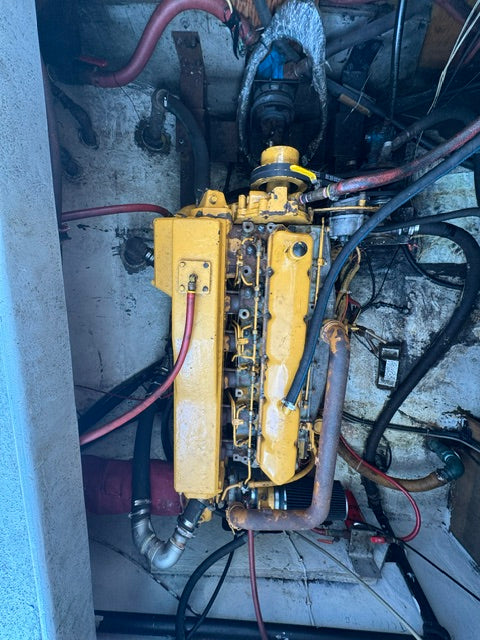 A used yellow marine engine mounted inside a boat's engine compartment, surrounded by hoses, pipes, and wiring.