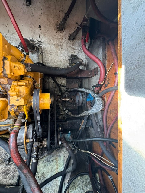A close-up view of a heavy-duty yellow industrial engine or machinery component with attached hoses, belts, and wiring inside a confined mechanical space.