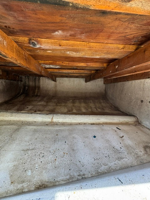 A narrow interior passage with weathered wooden beams and slats on the left and rough concrete walls on the right, viewed from within the space.