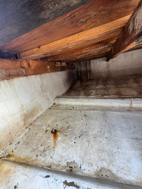 A narrow interior passage with weathered concrete walls and floor, alongside a rustic wooden structure on the left.