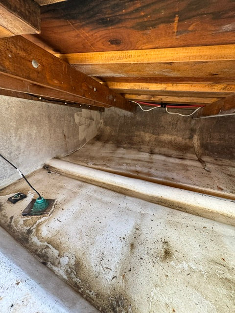 A narrow interior space with unfinished wood framing on the left, a concrete floor, and a textured concrete wall with a visible outlet and cord on the right.
