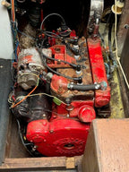 Close-up of a mechanical engine inside a wooden enclosure with visible wiring and tools.