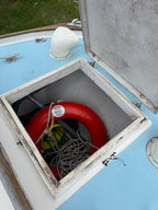 Red life buoy with a chain inside an open metal box on a blue wall.