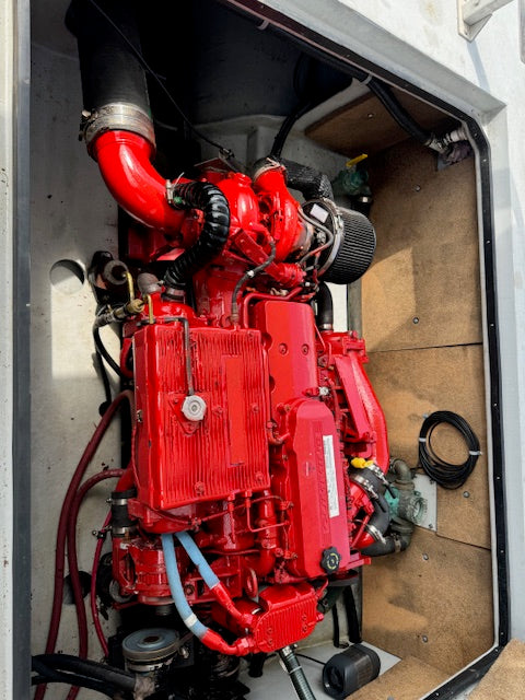 A red marine diesel engine installed in an open compartment, with black hoses, pipes, and wiring visible against a light-colored interior.