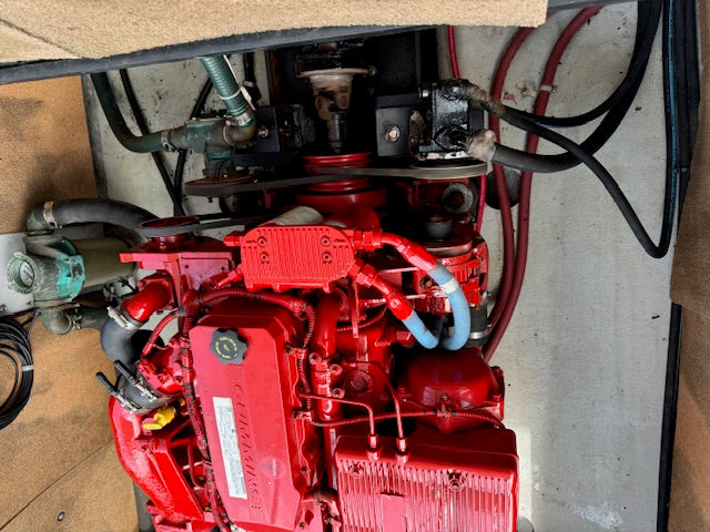 A red marine engine with various hoses, wires, and mechanical components visible, photographed from above inside what appears to be a boat or machinery compartment.