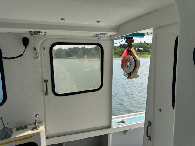 The interior of a boat cabin with a white door, window, and water view outside, featuring a red and white winch hanging from the ceiling.