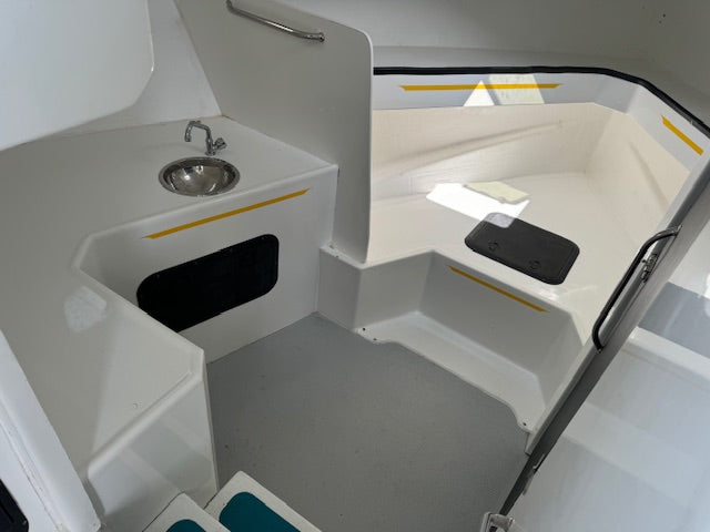 White molded fiberglass cockpit interior with a small sink, black storage compartment, gray floor, and yellow accent striping.