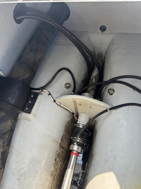 A close-up view of a marine or industrial mechanical setup inside a white compartment, featuring large cylindrical tanks or pipes, black cables, a metal fitting, and a small red ring detail.