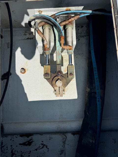 A close-up of a marine water suction pump assembly with metal cylinders, copper piping, and blue hoses inside a painted metal enclosure.