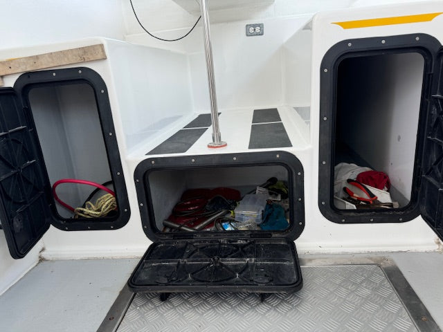 A white boat storage compartment with three open black-framed hatches, showing various gear and equipment stored inside, including a red coiled rope on the left and a black storage box on the floor.