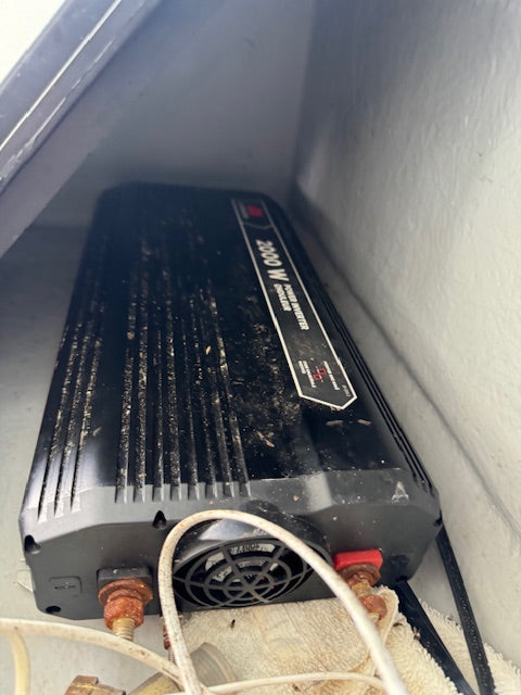 A dirty black marine inverter generator labeled 'INVERTER 300W' sitting in a tight space with wires and a white wall visible.