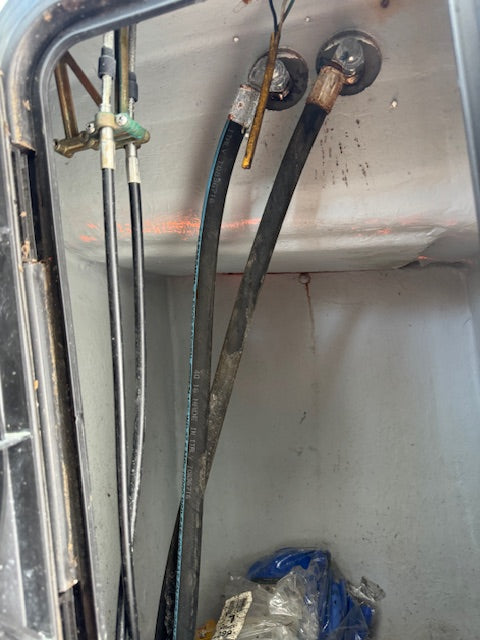 Close-up of industrial or marine equipment showing thick black hoses connected to metal fittings on a gray metal panel, with additional pipes and a small blue plastic bag visible at the bottom.