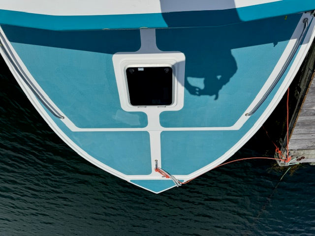 Top-down view of a boat's bow painted in light blue and white, moored at a dock with dark water and a wooden pier visible.