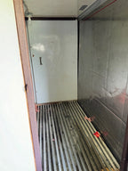 The interior of a commercial refrigerator or freezer compartment, showing a white door with a handle, a stainless steel slatted floor, and a textured metallic side wall.