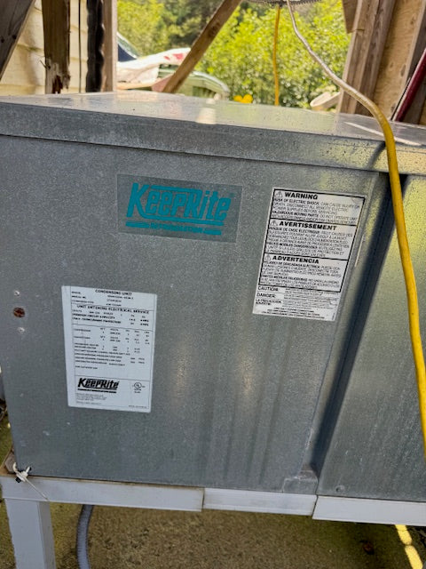A large galvanized steel Kool-Flite duct or equipment housing with attached labels, photographed in a real workshop/outdoor setting with visible wires and background structure.