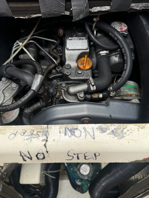 A close-up view of a used marine engine, likely a Volvo Penta, with handwritten markings on a white bar reading 'NON NO STEP'. The engine bay contains various black hoses, metal components, and an orange dipstick cap.