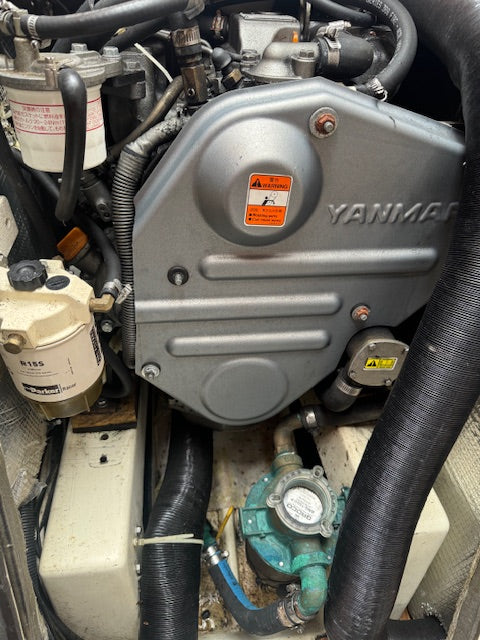A close-up view of a Yanmar marine engine, showing the large silver engine cover with the Yanmar logo, connected hoses, filters, and mechanical components.