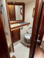 A compact bathroom interior with a white toilet, white sink and mirror, dark wood cabinetry, and a shower fixture on a beige floor.