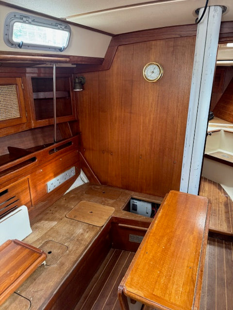 The interior cabin of a wooden boat featuring warm brown wood paneling, a wooden table, a wooden bench, and a round wall clock.