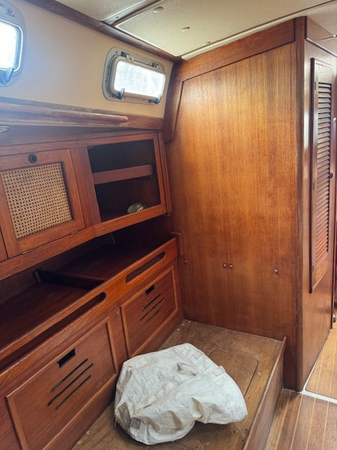 Wooden interior cabin space with storage cabinets, a slatted door panel, and a crumpled white fabric or bag on the floor.