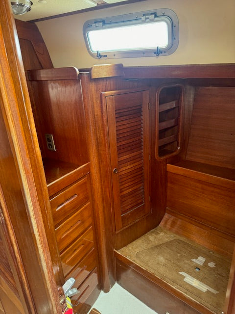 Wood-paneled interior cabin space with drawers, shelving, a louvered door, and a porthole window.