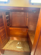 An interior wooden cabin space with wood-paneled walls, a bench or seat, a small shelf, and a floor hatch, photographed from inside the compartment.
