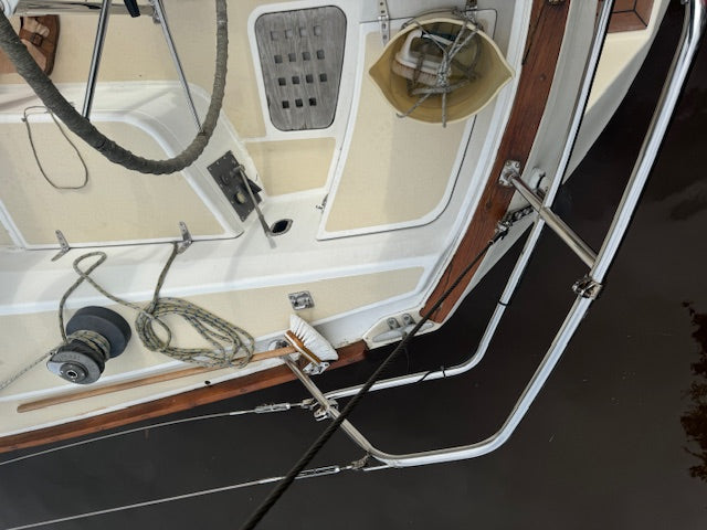 An overhead view of a boat's deck and cabin area, showing white fiberglass surfaces, dark wood trim, ropes, winches, and metal rigging over dark water.