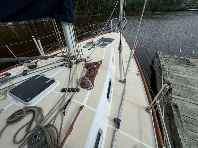 The deck of a sailboat docked at a wooden pier next to calm water, showing navigation equipment, ropes, and a dark blue canvas cover.