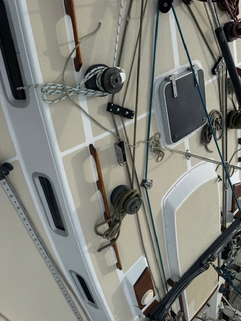 Close-up of a sailboat deck rigging setup with winches, ropes, cleats, and hardware attached to a cream-colored fiberglass hull.