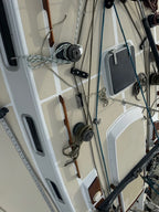 Close-up of a sailboat deck rigging setup with winches, ropes, cleats, and hardware attached to a cream-colored fiberglass hull.