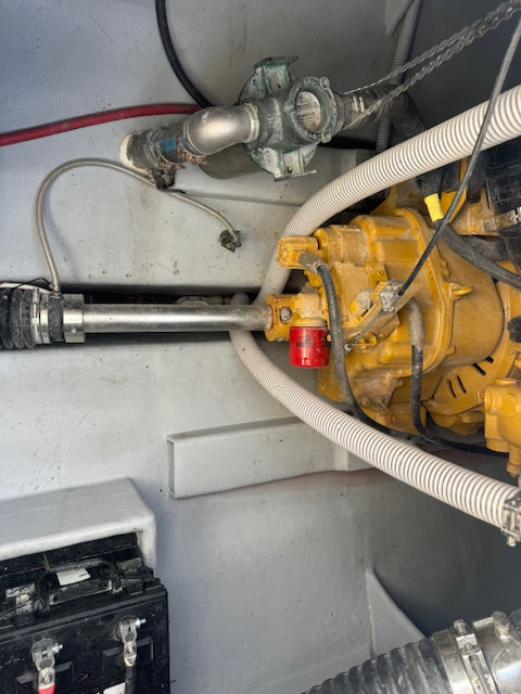 Close-up of a yellow industrial engine or pump assembly with white corrugated hoses, metal pipes, and a gray compartment wall.