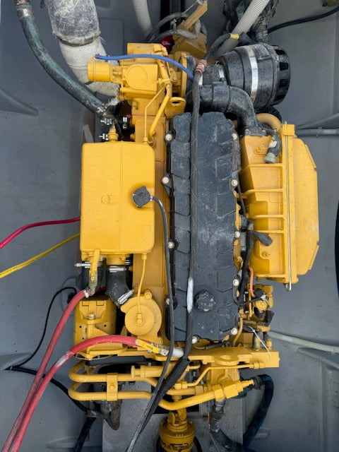 A yellow industrial engine or generator unit photographed from above, with black hoses, wires, and a large black ribbed cover on a gray mechanical compartment.