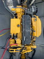 A yellow industrial engine or generator unit photographed from above, with black hoses, wires, and a large black ribbed cover on a gray mechanical compartment.