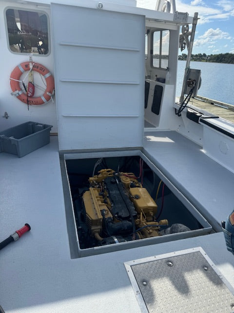 A yellow boat engine housed in an open hatch on the deck of a white boat, with water and shoreline visible in the background.