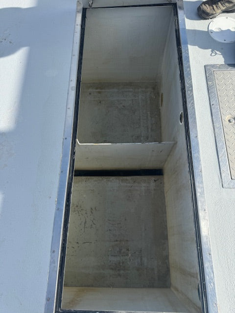 An open storage compartment or hatchway on a white boat or vessel, showing a divided interior with concrete-like walls and a metal frame.