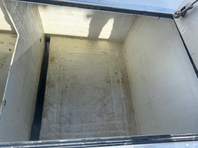 An empty, weathered metal storage bin or utility compartment viewed from inside, showing a concrete-like floor and painted metal walls with some dirt and wear.
