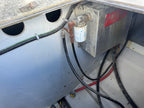 A close-up of a marine engine component, featuring a silver metal box with a red label, a white cylindrical filter, and various black and red hoses inside a boat cabin.