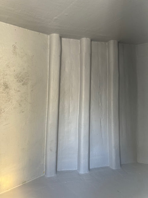 A set of light gray vertical fabric panels or curtains hanging in a corner of a room with a textured off-white plaster wall and ceiling.