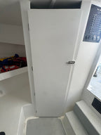 A white storage door with a silver handle, situated in a boat cabin next to shelves and stairs.