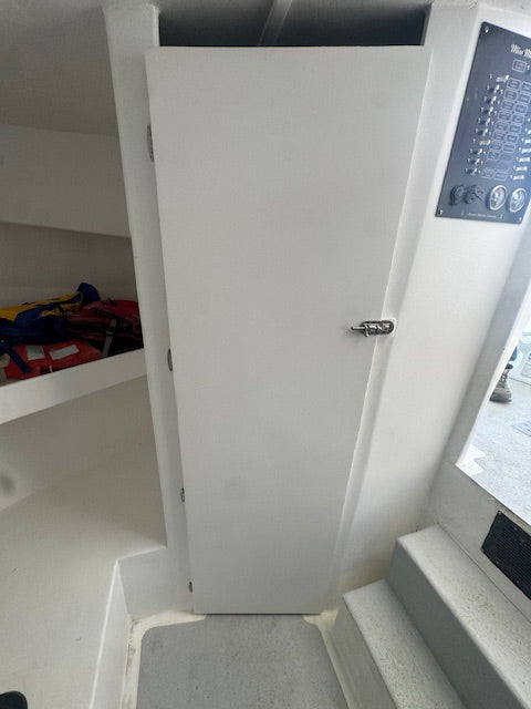 A white storage door with a silver handle, situated in a boat cabin next to shelves and stairs.