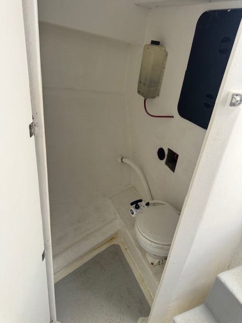 A small white toilet in a compact, utilitarian bathroom or galley space with white walls and a gray floor.