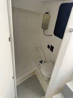 A small white toilet in a compact, utilitarian bathroom or galley space with white walls and a gray floor.
