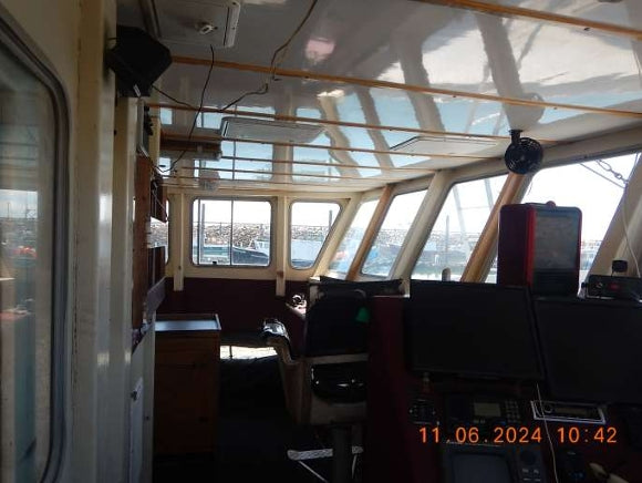 The interior of a boat's navigation bridge with windows, control screens, chairs, and a digital timestamp in the bottom right corner.