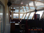 The interior of a boat's navigation bridge with windows, control screens, chairs, and a digital timestamp in the bottom right corner.