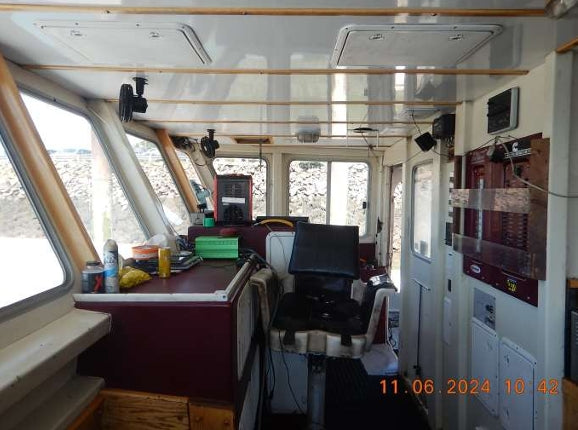 The interior of a boat cabin with a navigation station, helm seat, instrument panels, and storage cabinets. The photo is taken from within the cabin looking towards the navigation console and windows.
