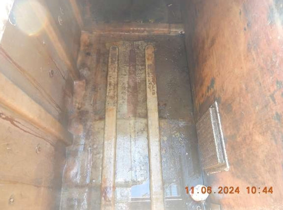 A dirty, rusty metal utility compartment or trench interior with vertical metal channels, wet concrete floor, and a small metal panel on the right side. A timestamp in orange is visible in the bottom right corner.